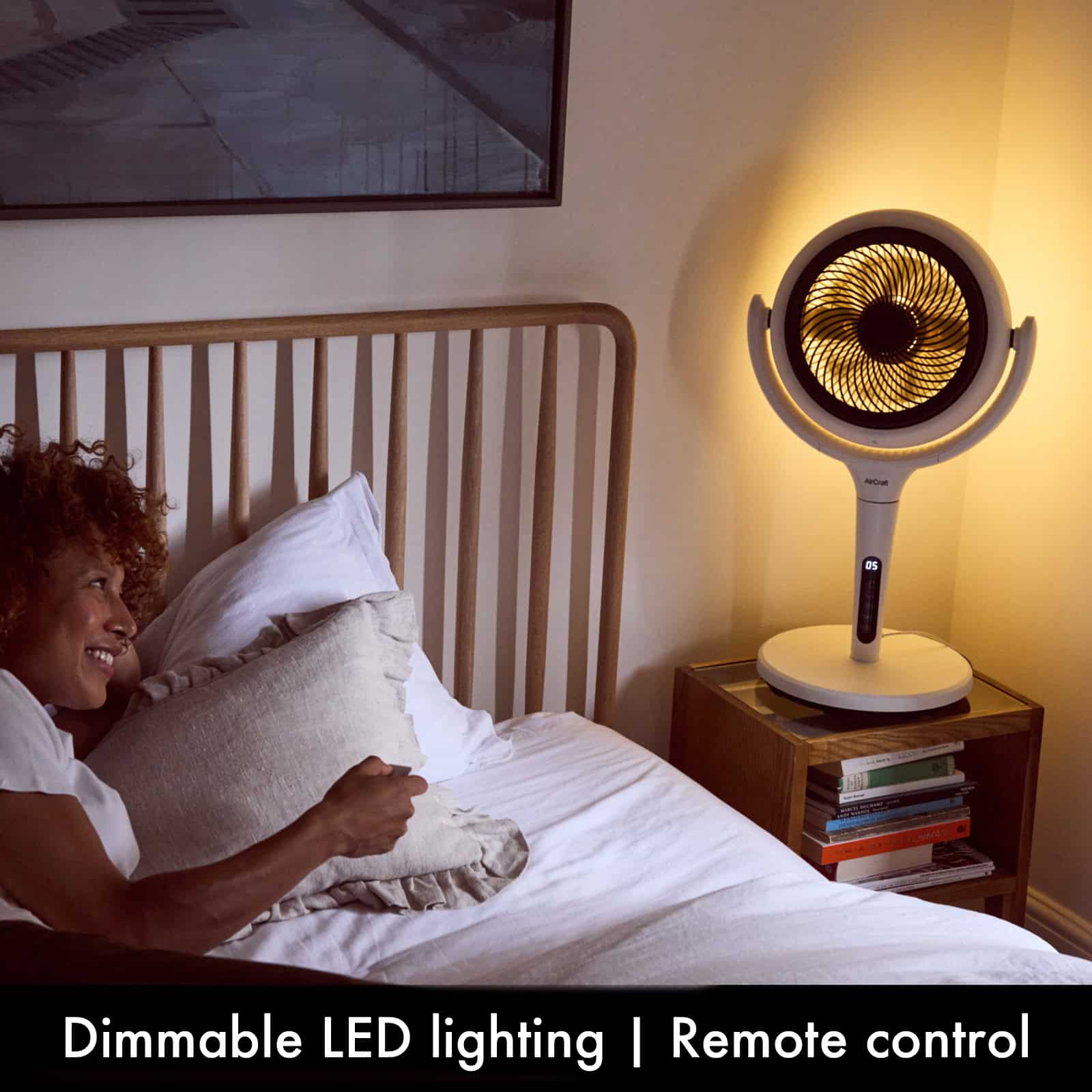 Girl in bed with remote controlled illuminated AirCraft LUME fan on bedside table